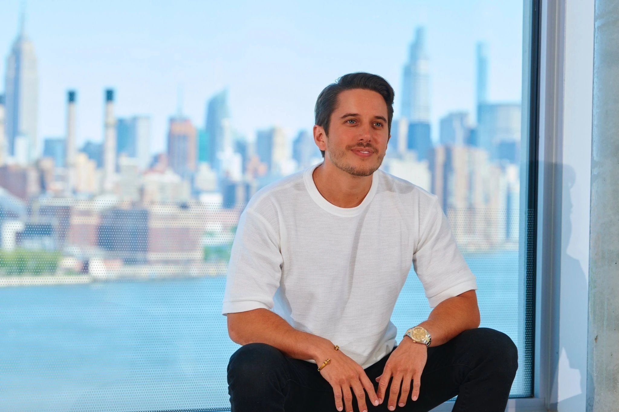 Oliver Yonchev seated by a large window with a city skyline in the background
